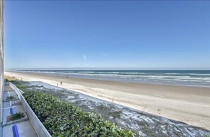 A beach view from a balcony with a railing, a clear sky, and the ocean.