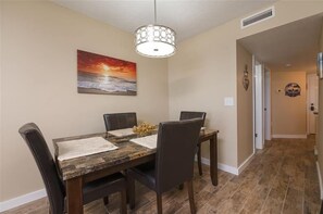 A dining area with a wooden table, four chairs, a decorative light fixture, and a painting of a sunset. - Welcome to Beach Life! 106 South Point " traffic free beach" (Ponce Inlet)