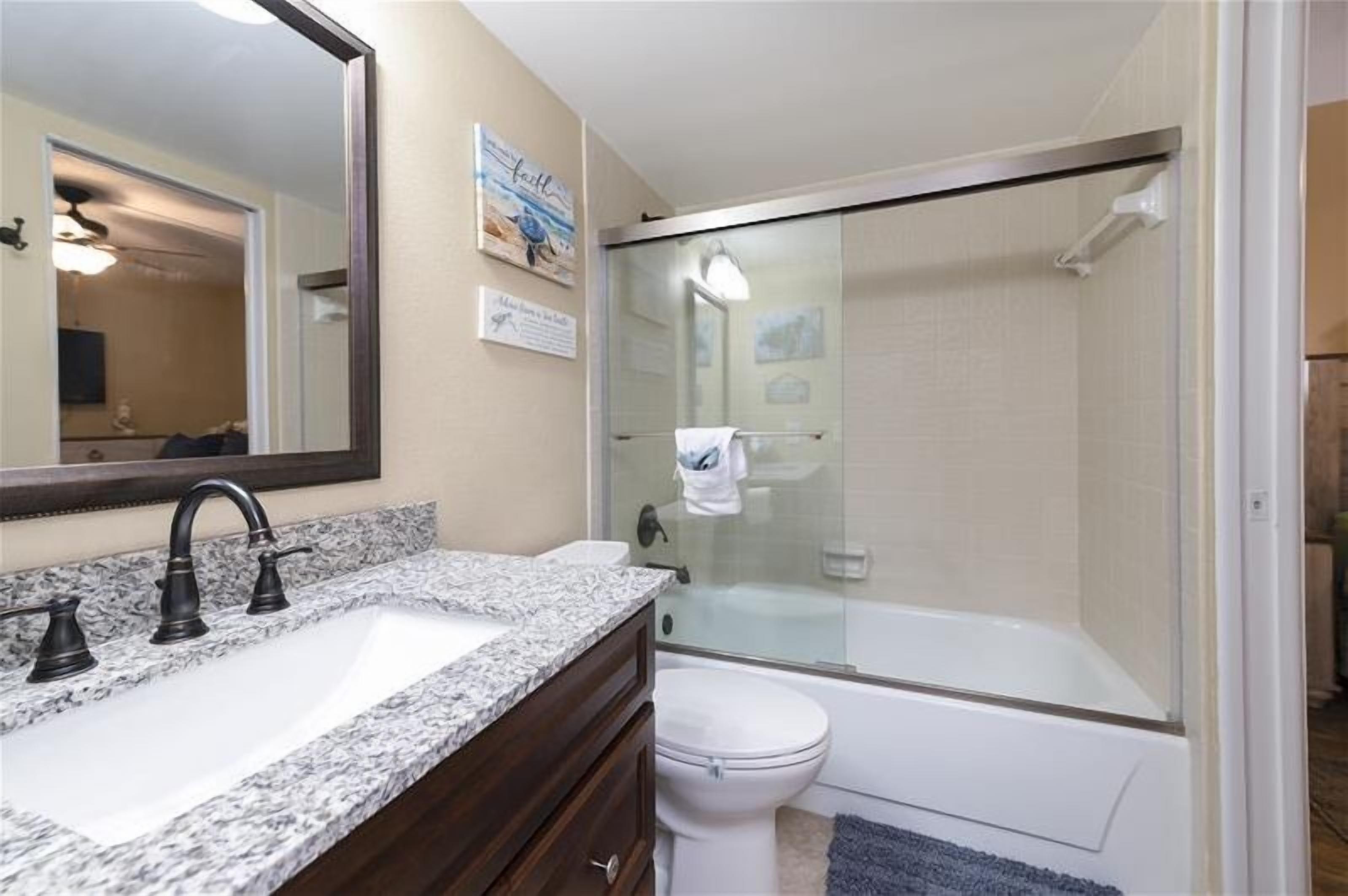 A bathroom with a granite countertop sink, a large mirror, a glass-enclosed shower, and a white toilet.