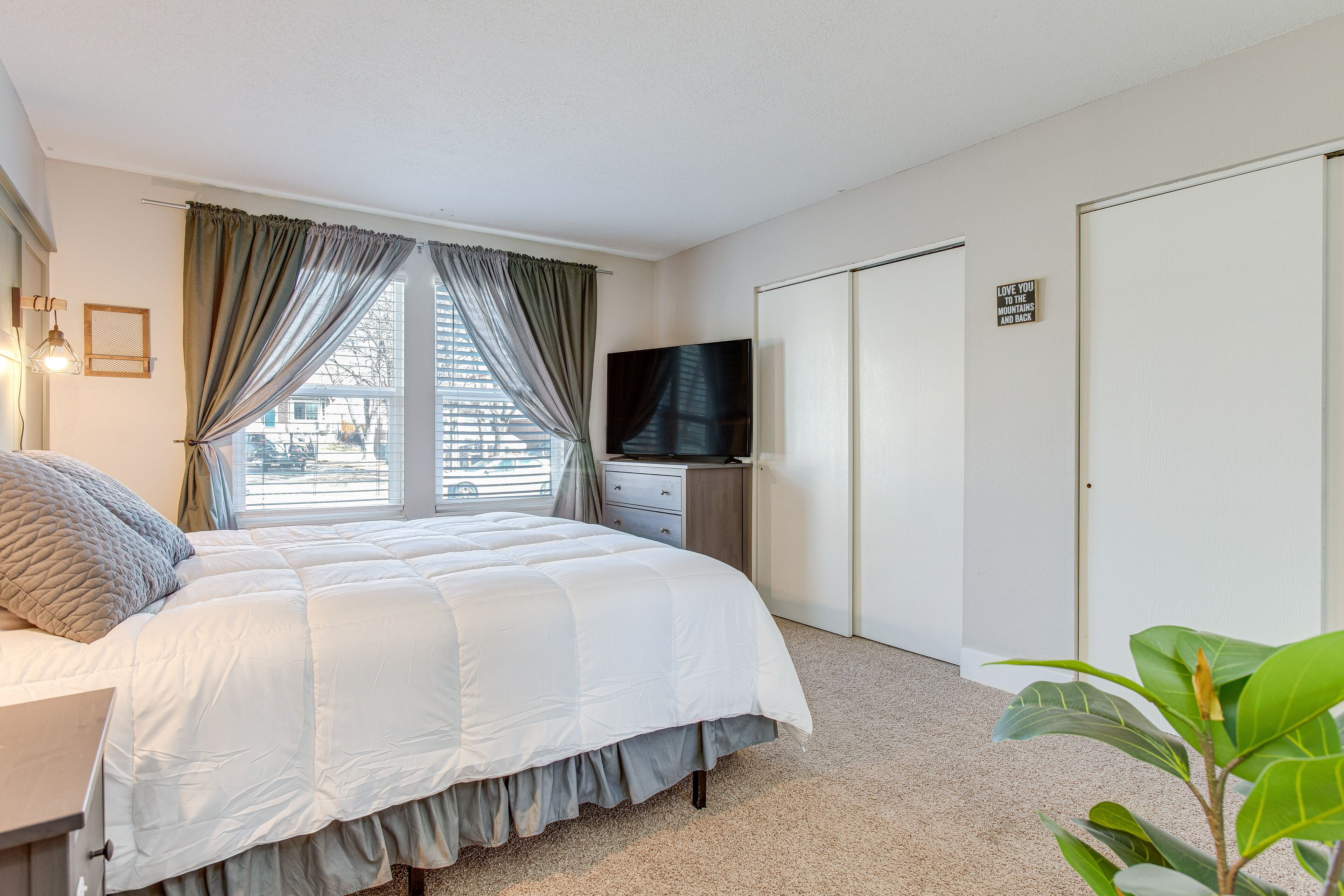 Une chambre à coucher avec un lit, une télévision, une armoire et une fenêtre avec des rideaux.