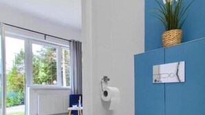 Un baño moderno con inodoro blanco, pared decorada en azul y una planta en maceta.