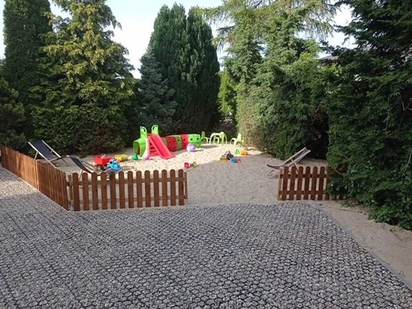 A playground with a slide and climbing structures surrounded by trees.