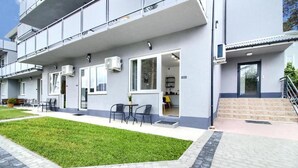 Un edificio moderno con techo plano, amplios ventanales y una pequeña zona exterior con sillas y mesas.
