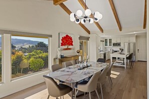Una cucina moderna con mobili bianchi, un'area pranzo con tavolo in marmo e vista su un paesaggio montano.