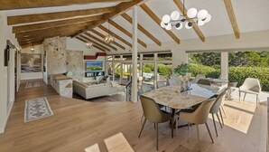 Ampla sala de estar com mesa de jantar, móveis modernos e janelas grandes com vista para o exterior.