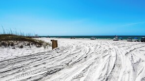 A sandy beach with tire tracks, a wooden sign, and vehicles parked near the water.