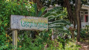 A wooden sign with "WELCOME TO GRYNY BEACH" written on it, surrounded by lush greenery and palm trees.