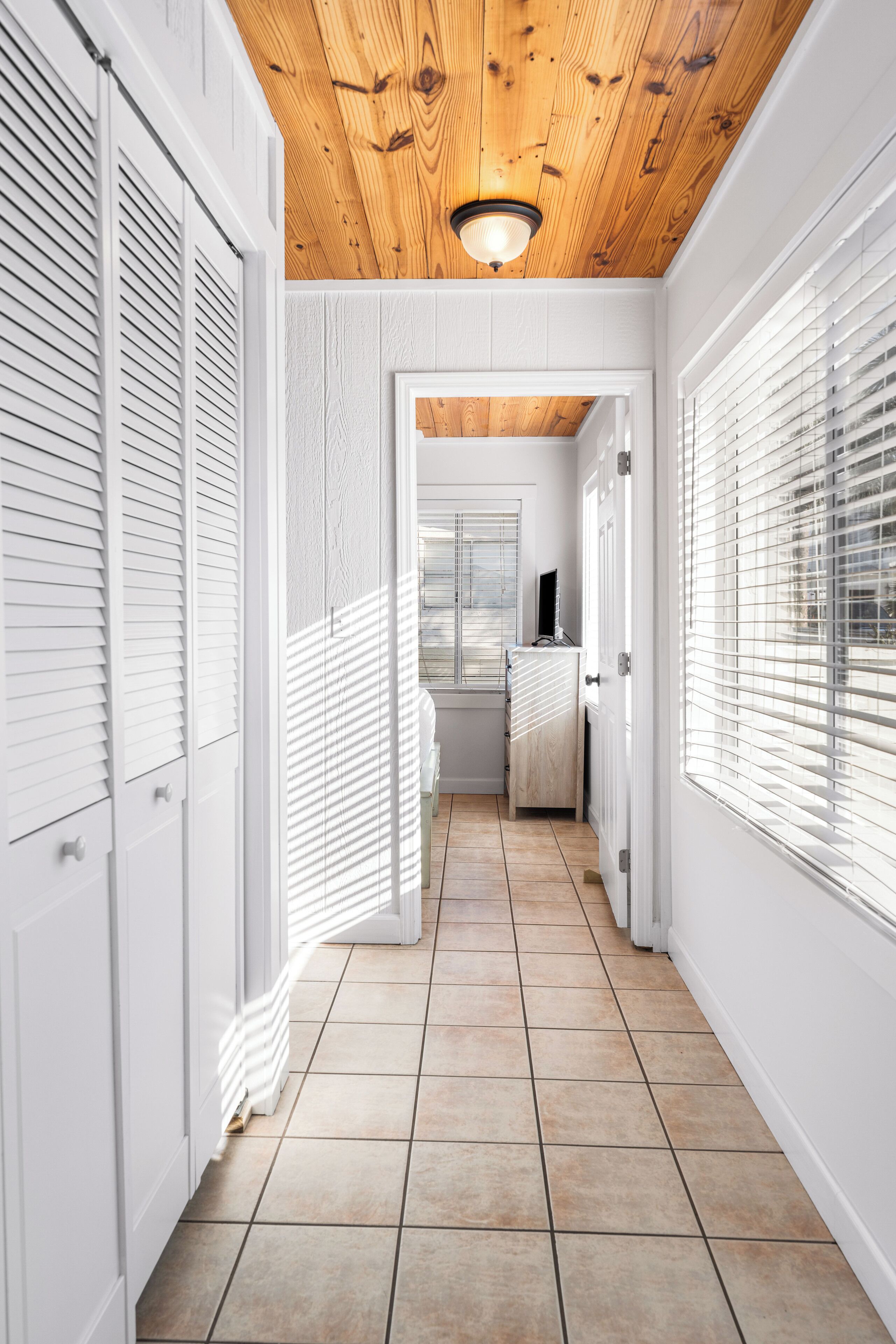 A hallway with white walls, wooden ceiling, and tiled floor.