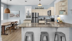A modern kitchen with a central island, stainless steel appliances, and a 'BEACH HOUSE' sign. - Dog Friendly, Close to Beach, Overlooks Pool/Spa + Free Attraction Tickets! (Santa Rosa Beach)