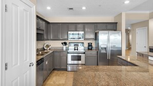Una cocina moderna con electrodomésticos de acero inoxidable, encimeras de granito y armarios grises.
