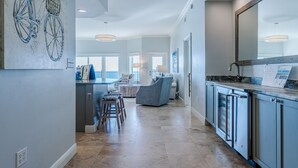 A modern kitchen with a large island, a dining area with a high chair, and a living room with a sofa and a large window. - Gulf-Front, Lovely Views & Private Beach, Sleeps 12 + Free Attraction Tickets (Seagrove Beach)