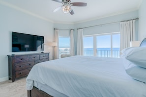A bedroom with a large bed, a ceiling fan, a TV, and a view of the ocean.