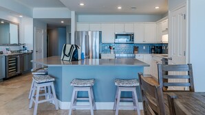 A modern kitchen with white cabinets, stainless steel appliances, and a blue island with bar stools. - Gulf-Front, Lovely Views & Private Beach, Sleeps 12 + Free Attraction Tickets (Seagrove Beach)