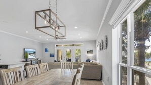 Een eetruimte met een houten tafel en stoelen, een hanglamp en uitzicht op het omliggende landschap door grote ramen.
