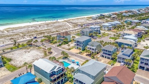 Un quartier résidentiel situé sur la côte, avec des propriétés donnant sur la plage, une piscine et une route menant à la plage.