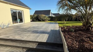 A wooden deck leading to a house with a sliding glass door. - Vacation home, 400m from the sea in a quiet, well-located area (Saint-Quay-Portrieux)