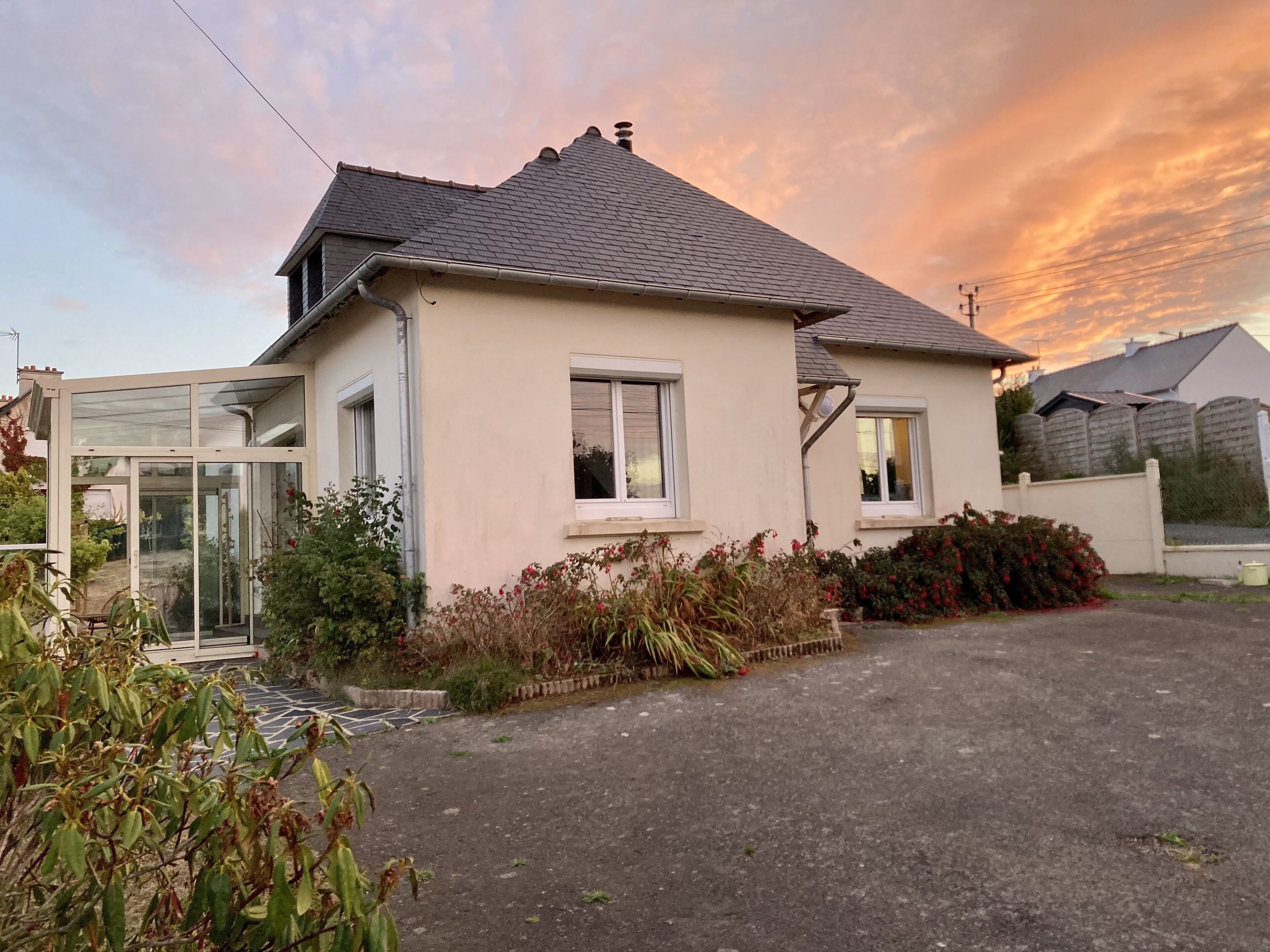 Une maison de plain-pied avec un toit en pente, une porte d’entrée en verre et une allée menant à l’entrée.