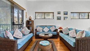 Un salón con muebles de mimbre, un sofá azul, una mesa de centro y cuadros en la pared.