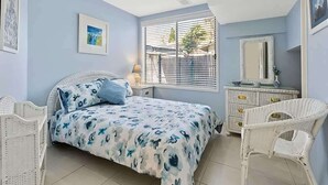 Un dormitorio con cama, cómoda, silla, ventana con persianas y un cuadro en la pared.