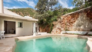 A swimming pool with a stone wall and a white building with a window. - Kaolin Rocabella Apartment with Private Sandy Pool (El Chorro)
