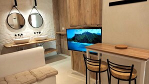 A modern bathroom with a large mirror, a sink, and a television displaying a scenic view. - Kaolin Rocabella Apartment with Private Sandy Pool (El Chorro)