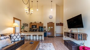 A living room with a sofa, coffee table, and a TV mounted on the wall. There is a kitchen area with a refrigerator, microwave, and bar stools. - Close to Gondola and Short Walk to Keystone Base Area Shops and Dining! (Keystone)