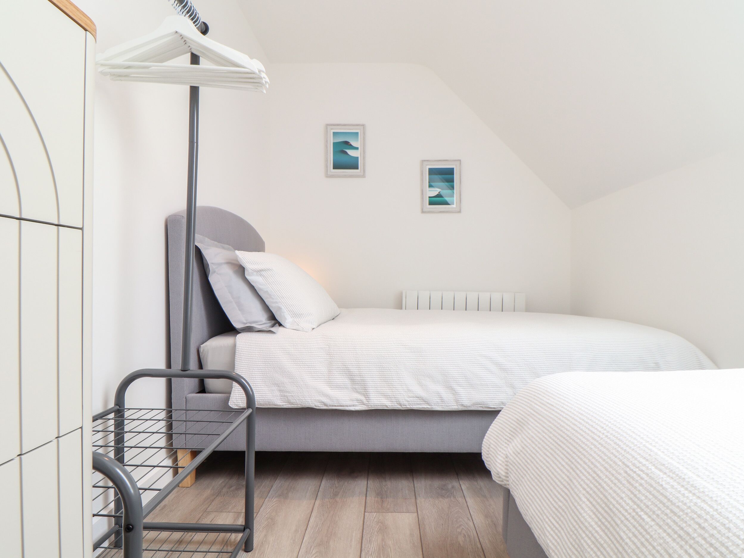 Une chambre à coucher avec un lit, une petite table de chevet, un radiateur et deux tableaux encadrés accrochés au mur.