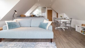 A modern loft apartment with a sloped ceiling, a sofa, a dining table, and a kitchen area. - Marazion Attic (Marazion)