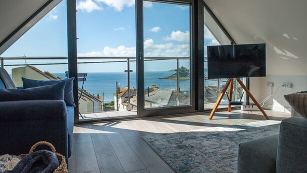A modern living room with a large sliding glass door leading to a balcony with a sea view. - Marazion Attic (Marazion)