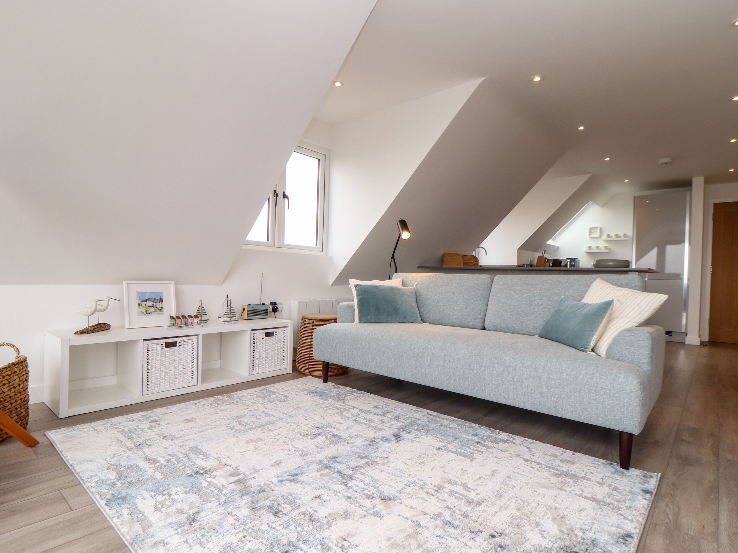 A modern loft bedroom with a grey sofa, a patterned rug, and a lofted kitchen area.