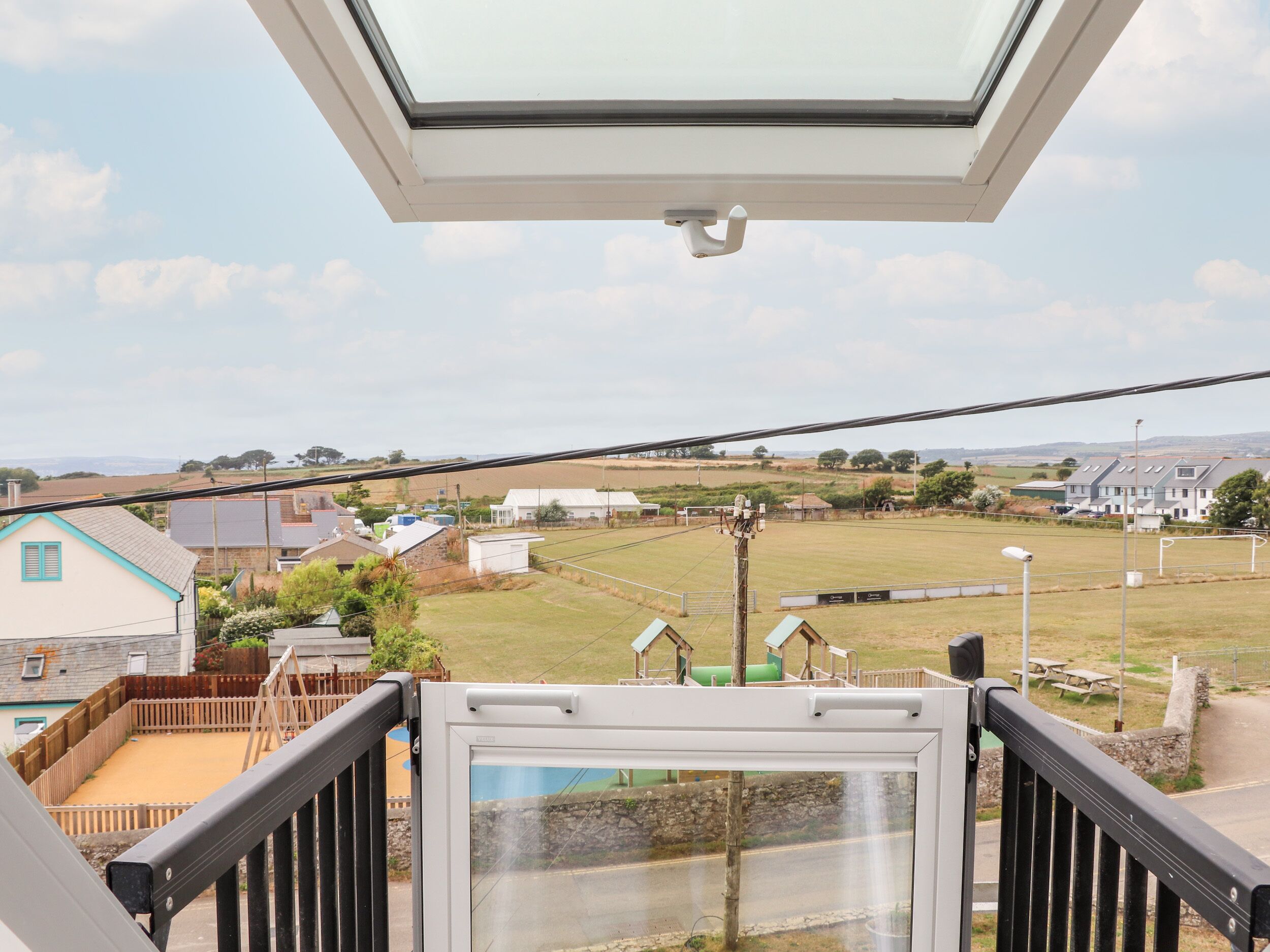 Un balcone con vista su un paesaggio rurale, tra case e campi aperti.
