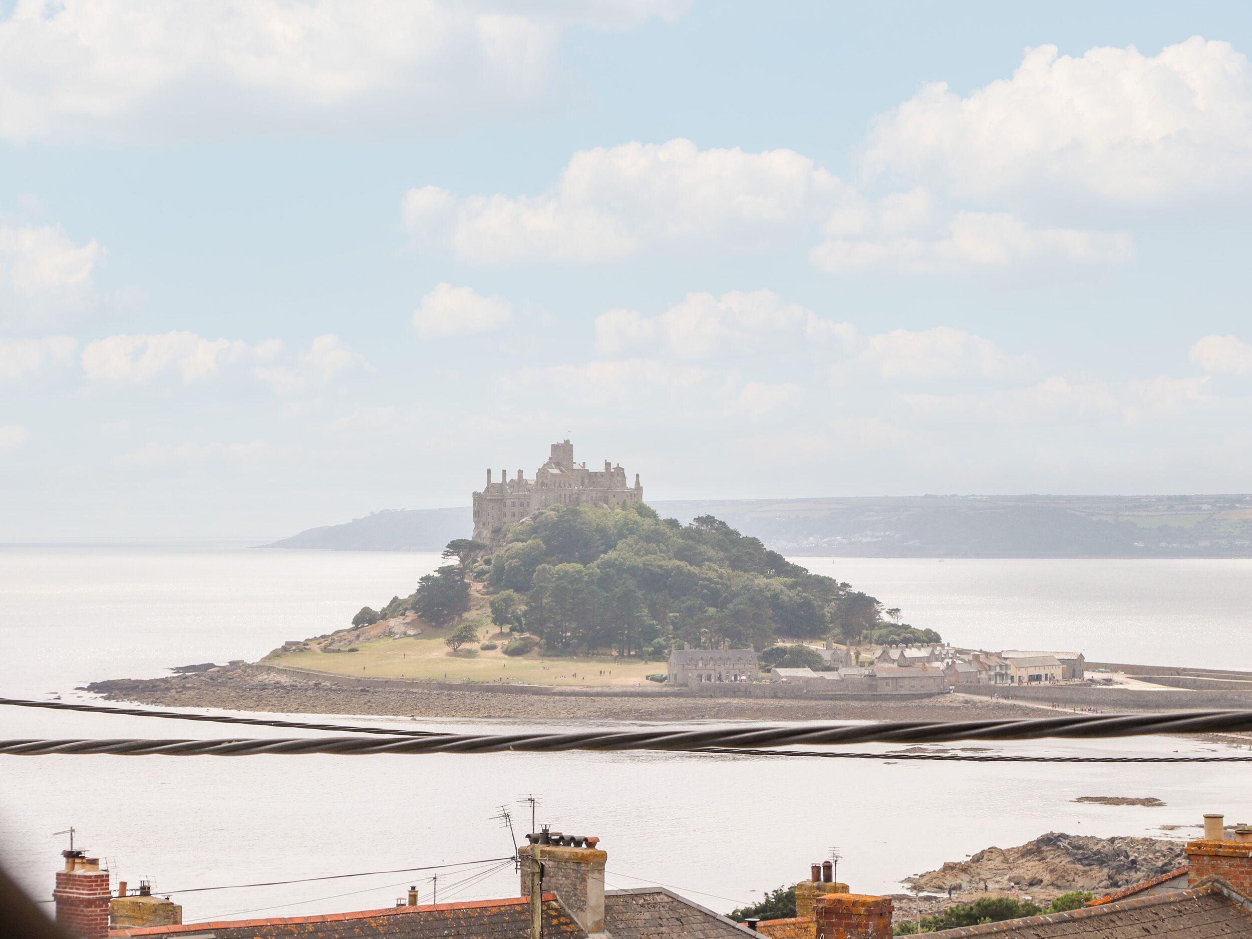 A coastal view with a castle on a small island, surrounded by water and distant buildings.