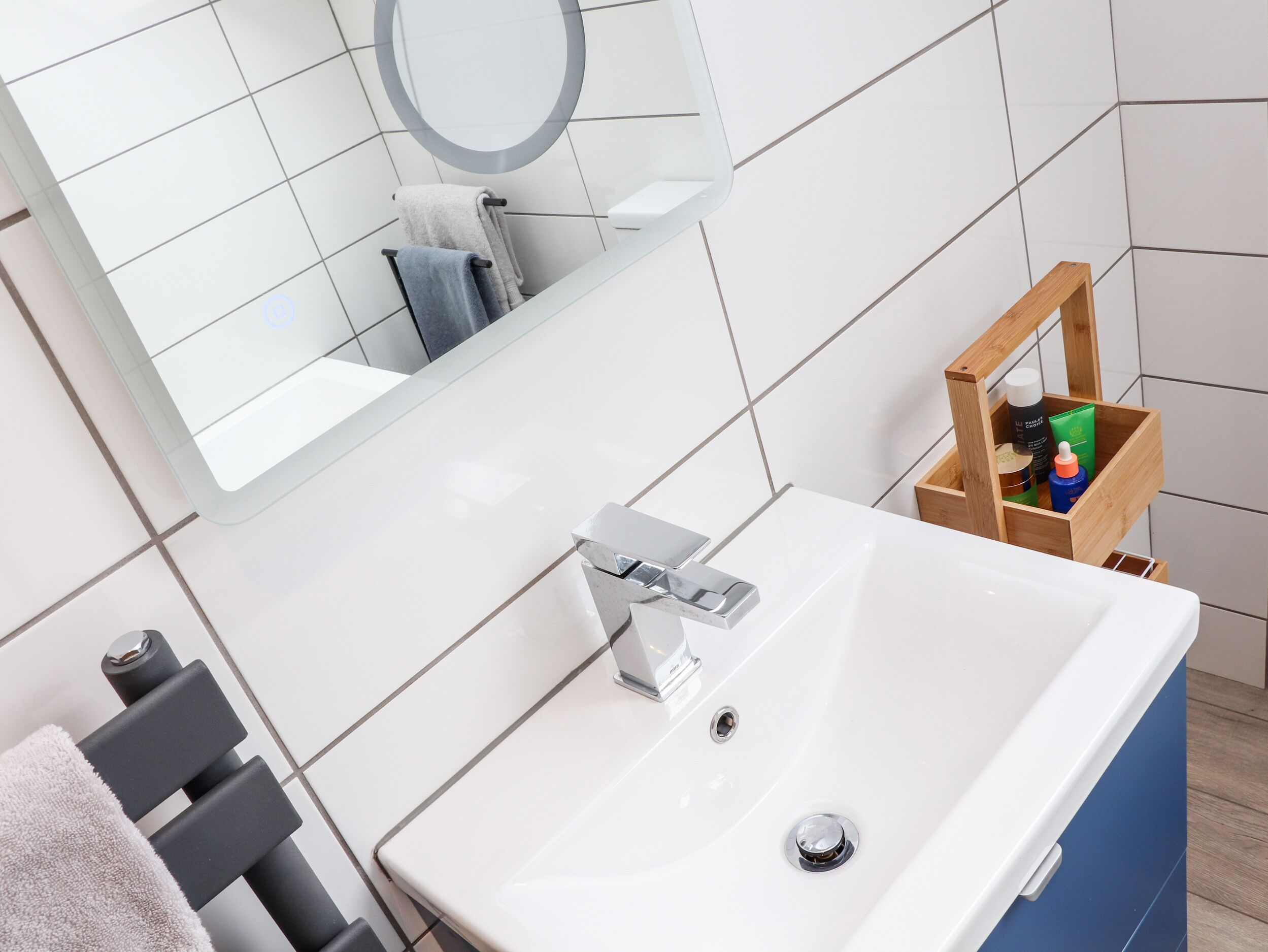 A bathroom with a white sink, a mirror, and a wooden storage box with toiletries.