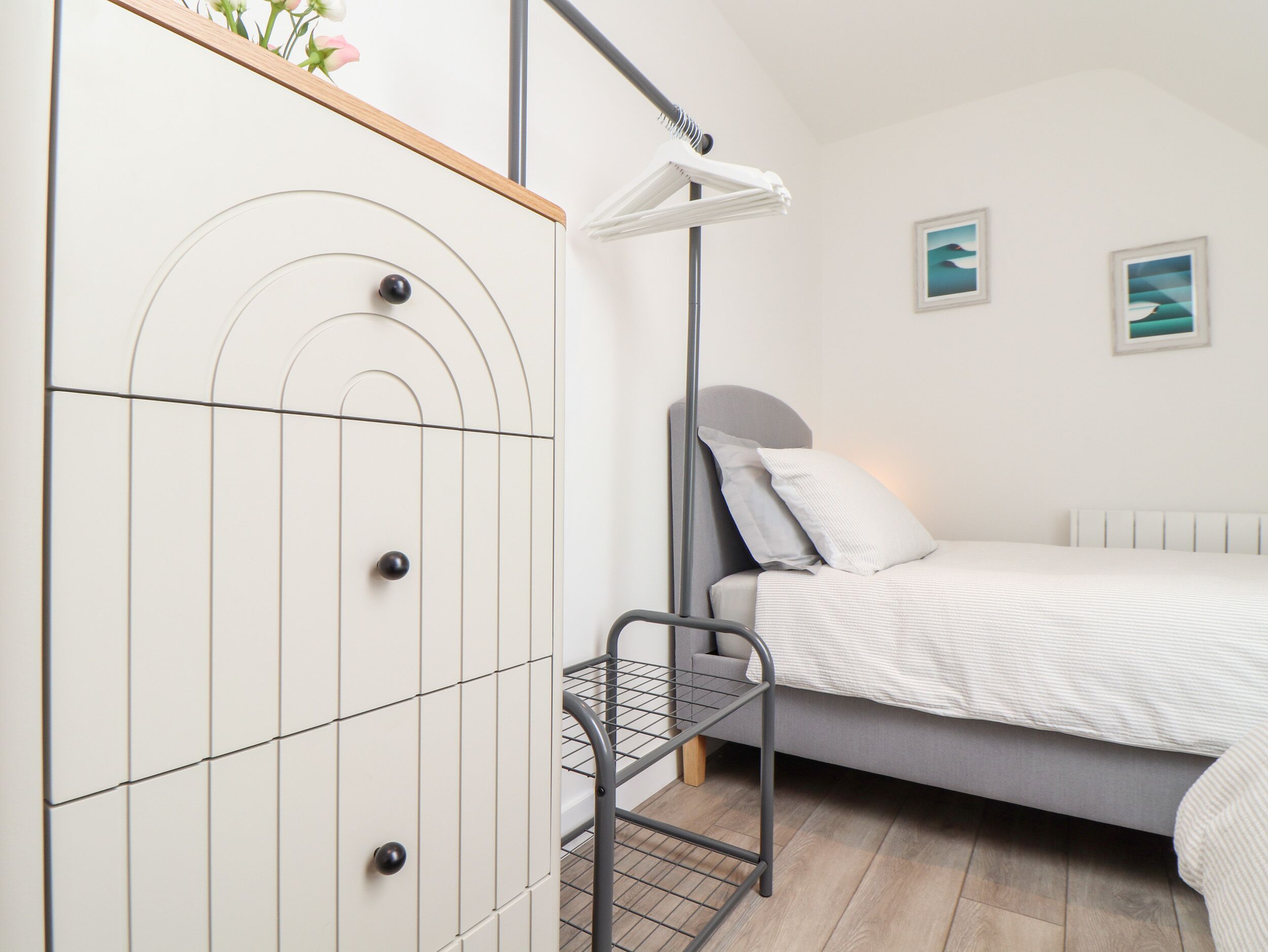 A bedroom with a bed, a wardrobe, a desk with a chair, and a hanging light fixture.