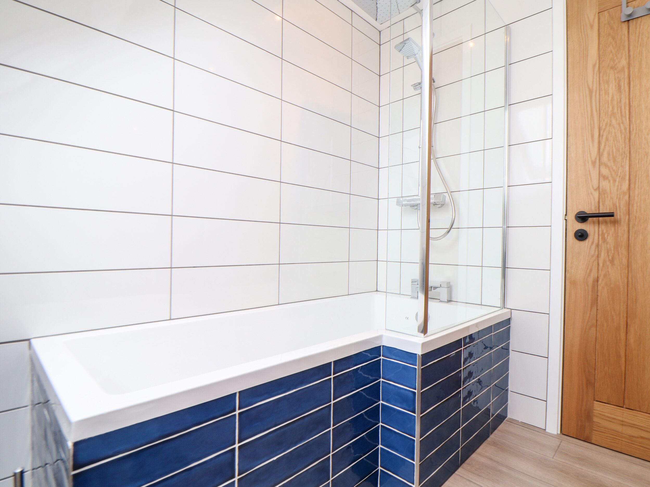Casa de banho com azulejos brancos e azuis, uma banheira e uma porta de madeira.