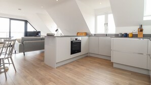 A modern kitchen with a dining area, featuring a kitchen island, built-in oven, and a dining table with chairs. - Marazion Attic (Marazion)
