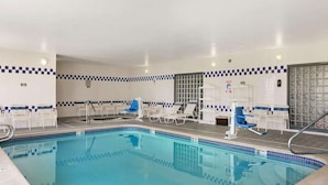 Ein Schwimmbecken mit blauen Fliesen, weißen Liegestühlen und einer Wand mit Schachbrettmuster.