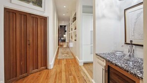 Un passadís amb paviment de fusta, una zona de cuina amb encimera de granat i una zona de menjador al fons.