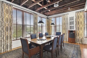 A dining area with a wooden table, six chairs, two pendant lights, and large windows with curtains.