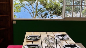 Mesa de comedor servida con platos y cubiertos, ubicada cerca de una ventana con vistas a árboles.