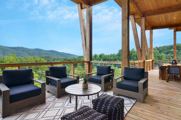 A wooden deck with outdoor furniture, including chairs and a table, overlooking a mountainous landscape. - Mountain View Manor  ~ Mountain Modern 5BR ~ Near downtown Blue Ridge! (Blue Ridge)