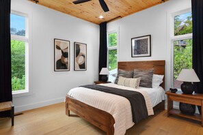 A bedroom with a wooden bed, two bedside tables, a window with curtains, and framed artwork on the wall. - Mountain View Manor  ~ Mountain Modern 5BR ~ Near downtown Blue Ridge! (Blue Ridge)
