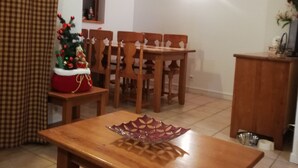 Zona pranzo con tavolo e sedie in legno, un piccolo albero di Natale e una finestra con tende.