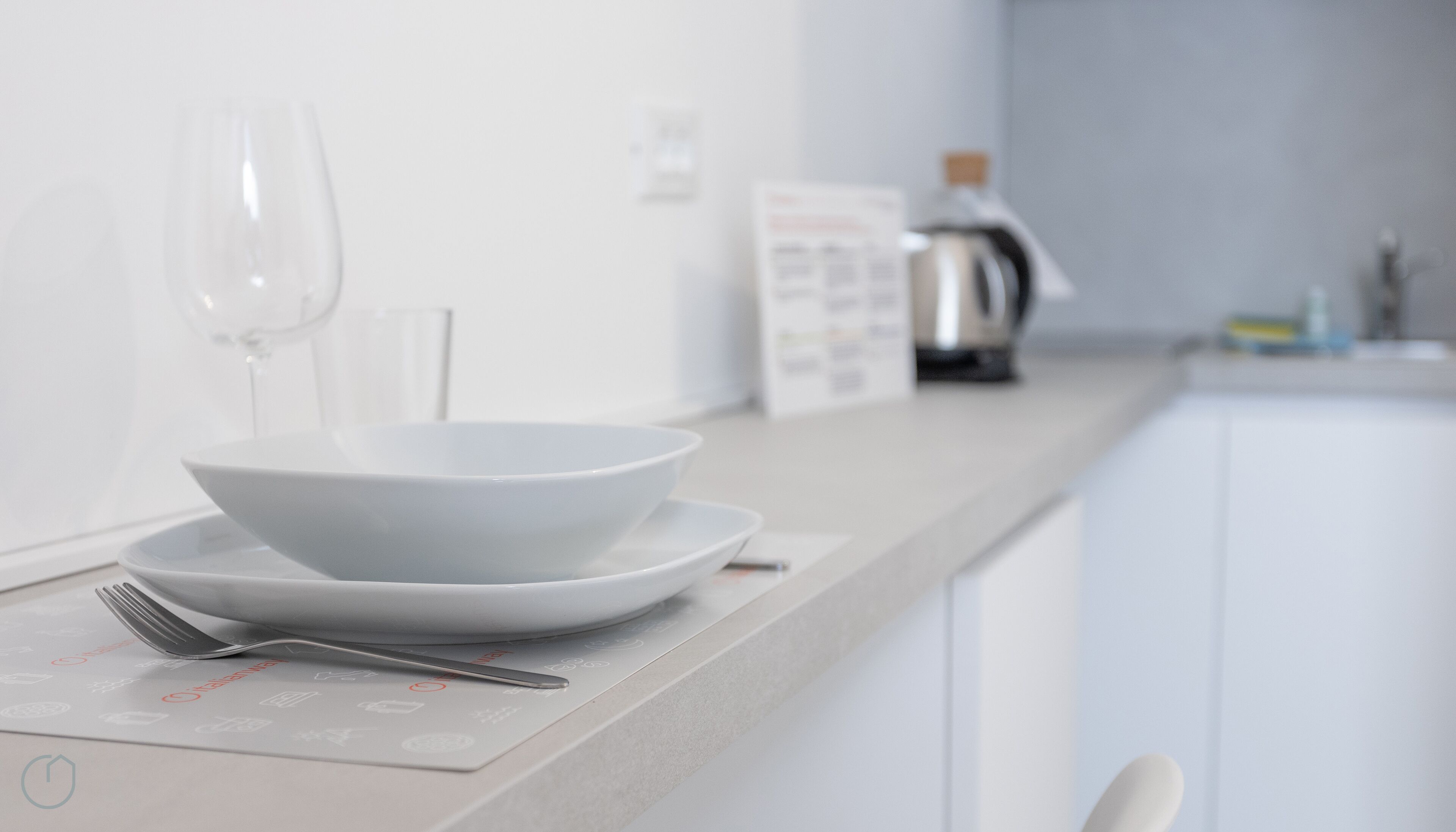 Una cocina moderna con encimeras blancas, una cafetera y una copa de vino.