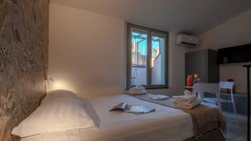 A hotel room with two beds, a window with a view of the outside, a flat-screen TV mounted on the wall, and a small table with a chair.