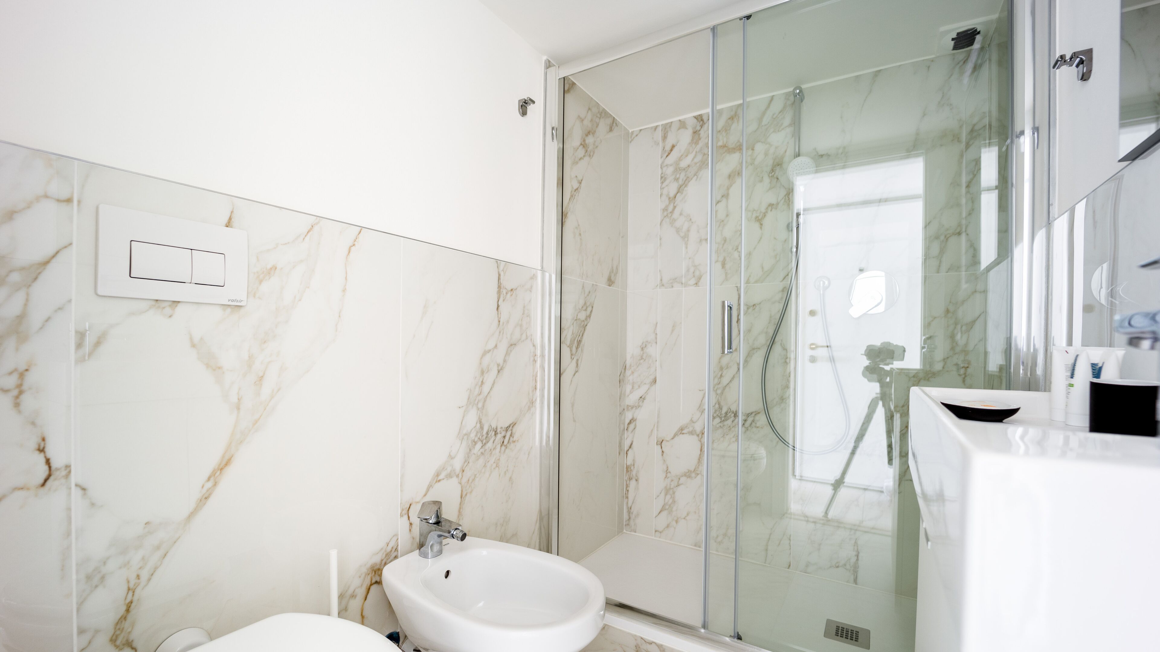 Ein Badezimmer mit Marmorwand, einer Duschkabine aus Glas, einem weißen Waschbecken und einem Bidet.