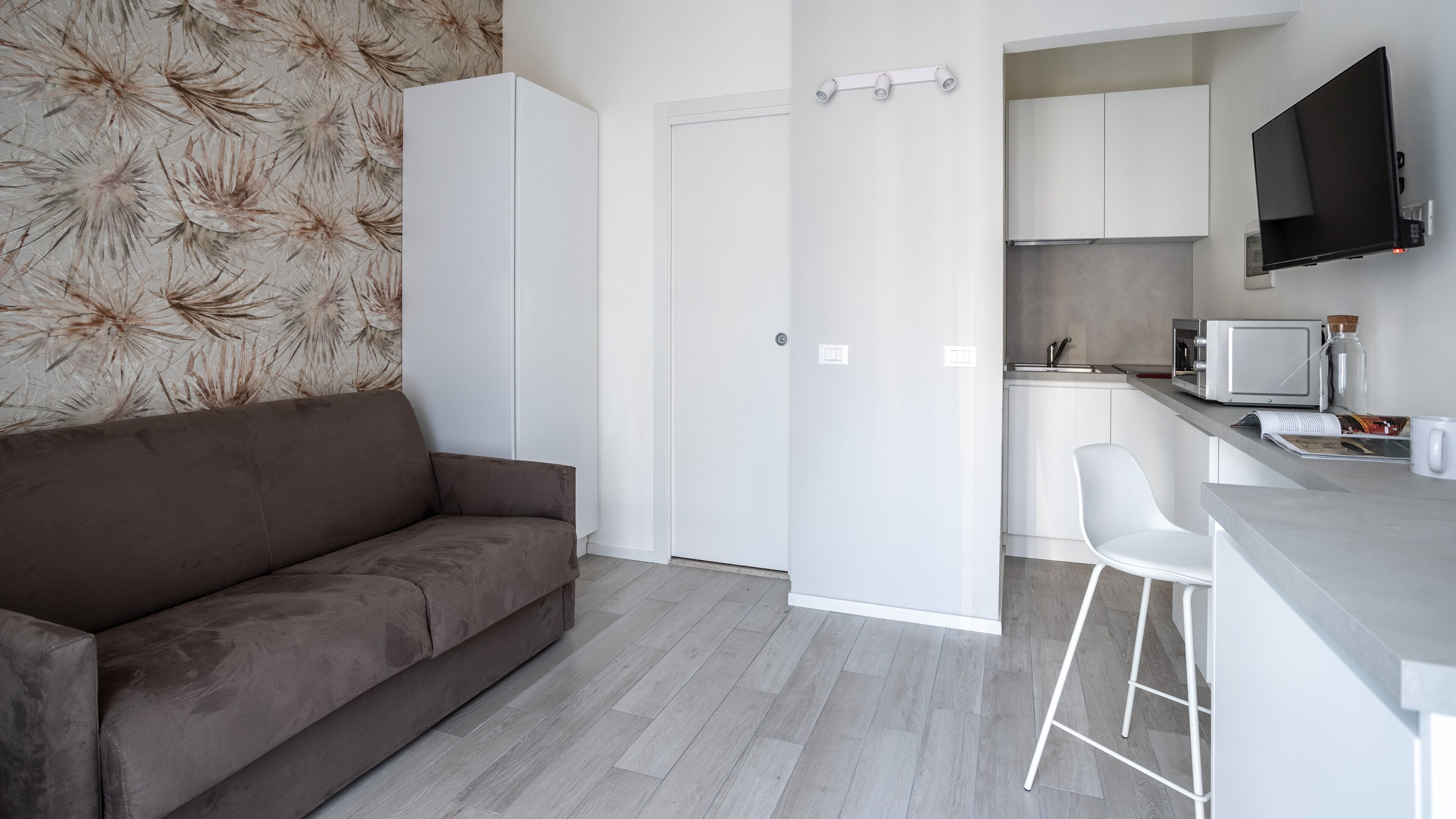 A modern kitchen with white cabinets, a built-in microwave, and a flat-screen TV mounted on the wall.