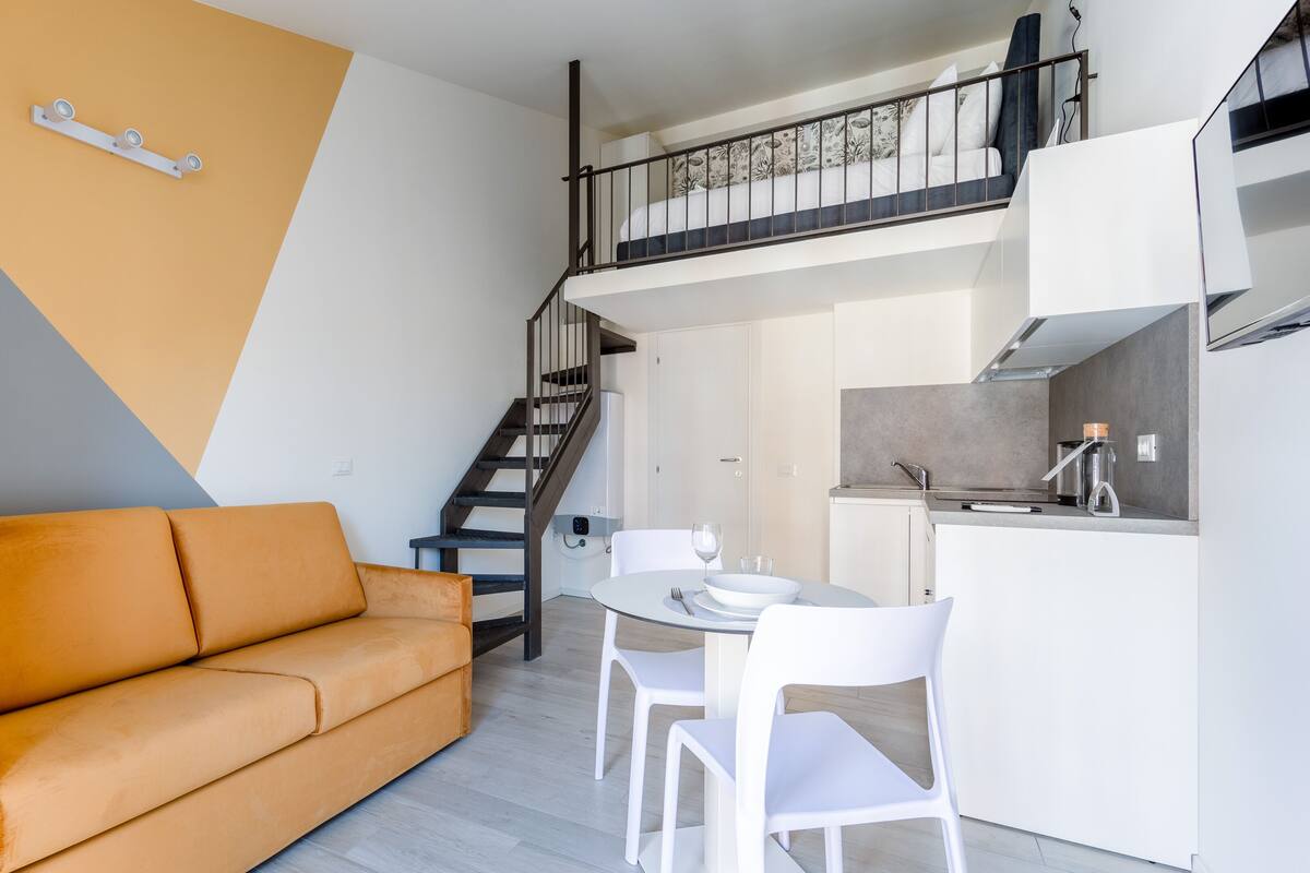 A modern apartment with a sofa, dining table, chairs, a kitchen, and a staircase.