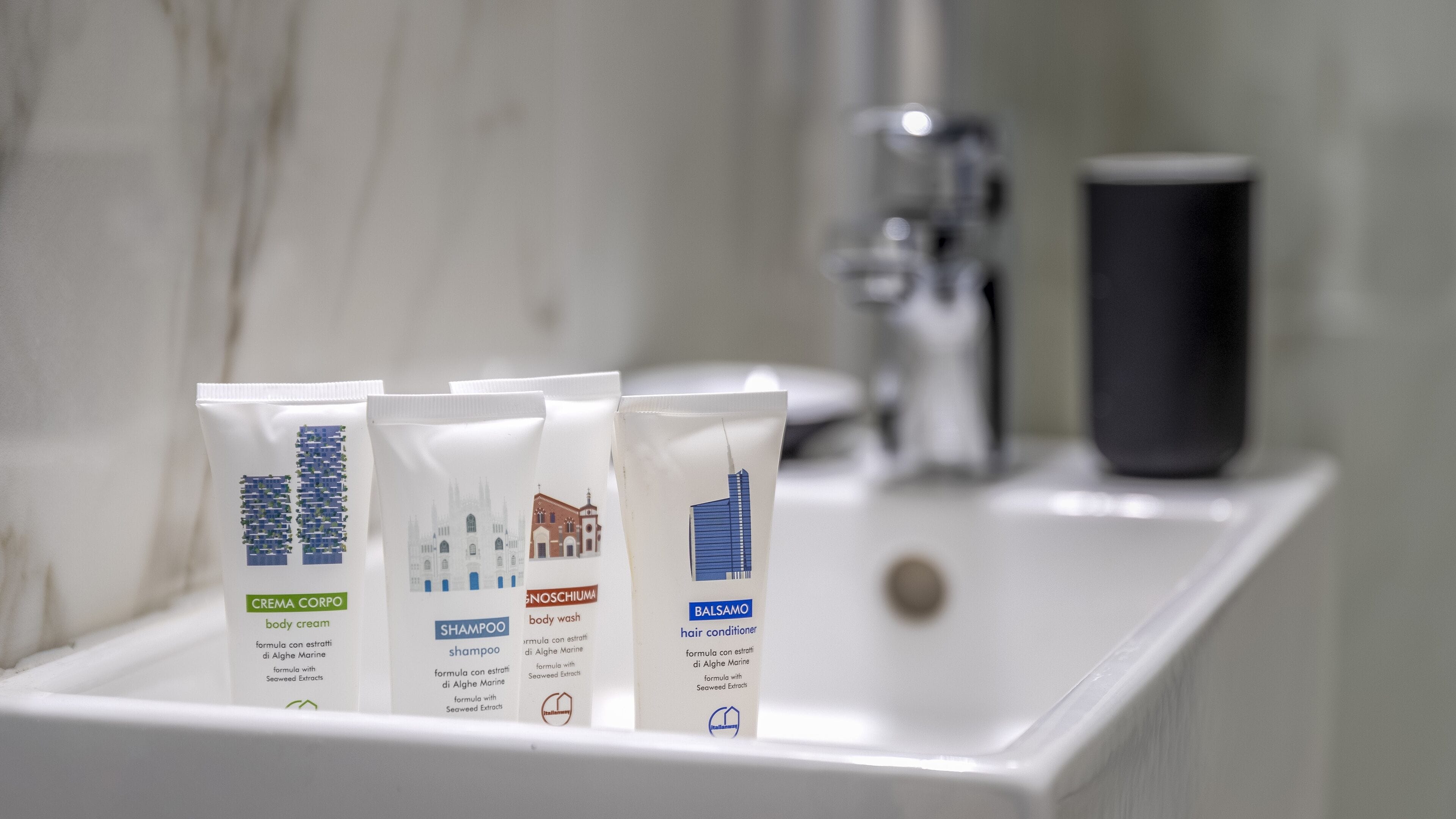 Tres artículos de tocador sobre un lavamanos de baño: crema corporal, champú y acondicionador para el cabello.