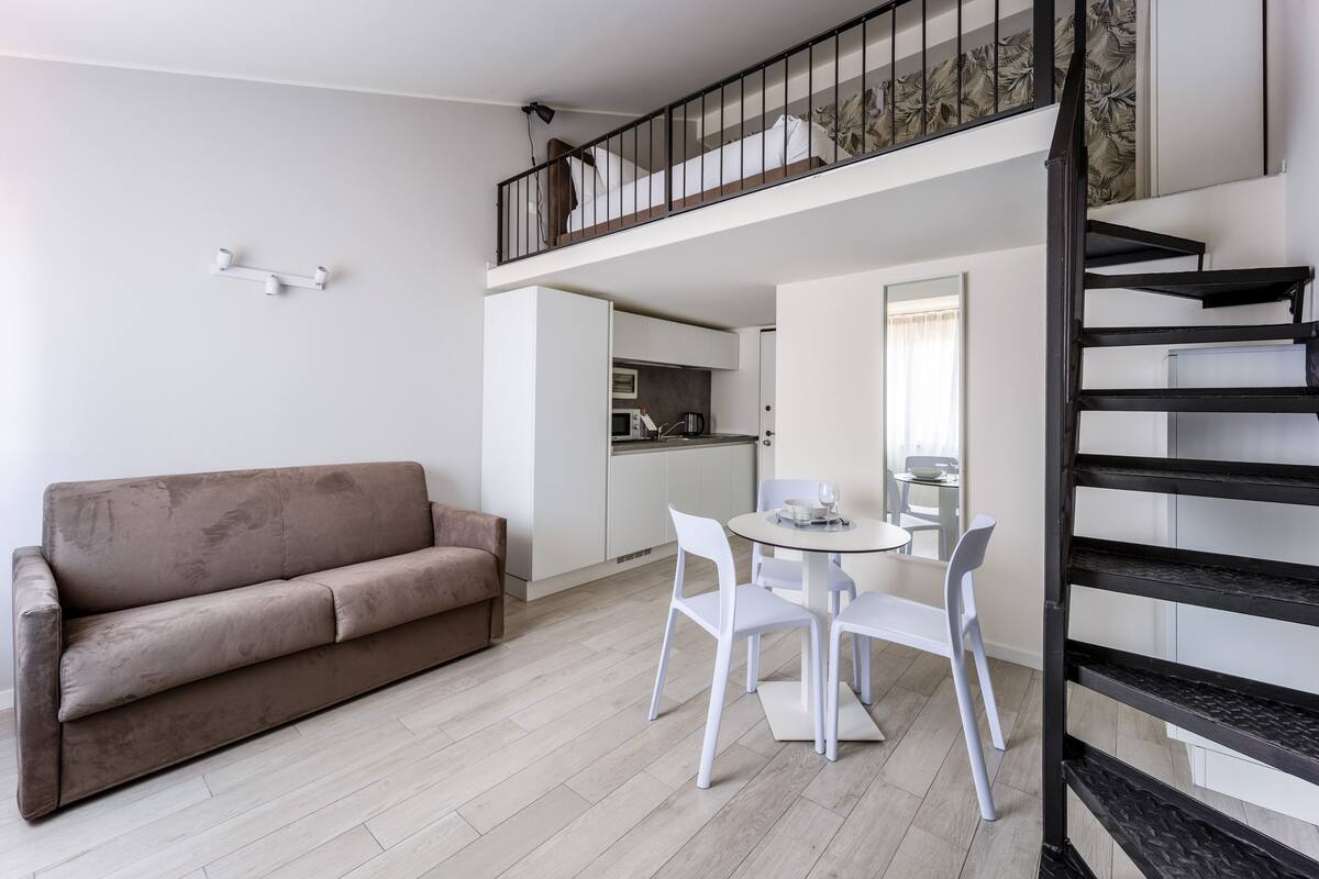 A modern living space with a sofa, dining table, chairs, and a staircase.